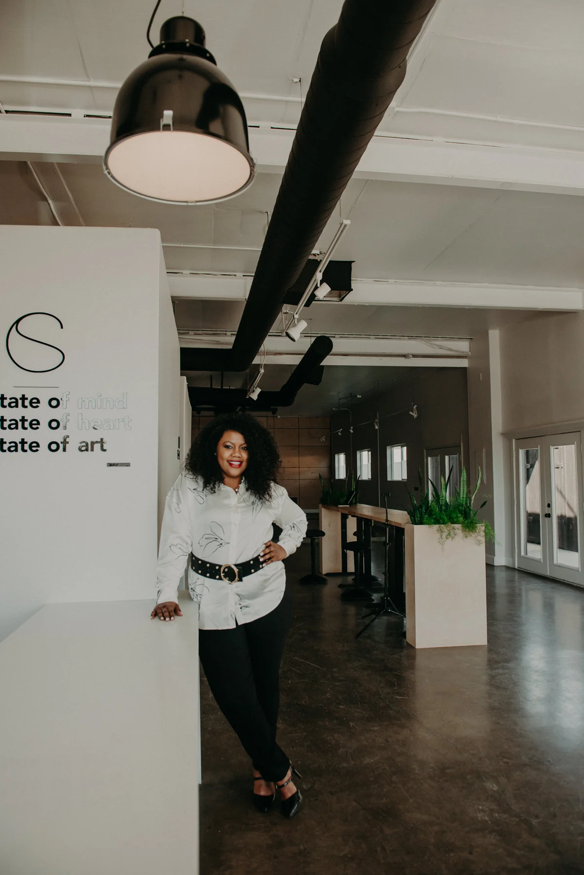 Irene Wilkins standing in a bright studio wearing a white patterned blouse and black trousers